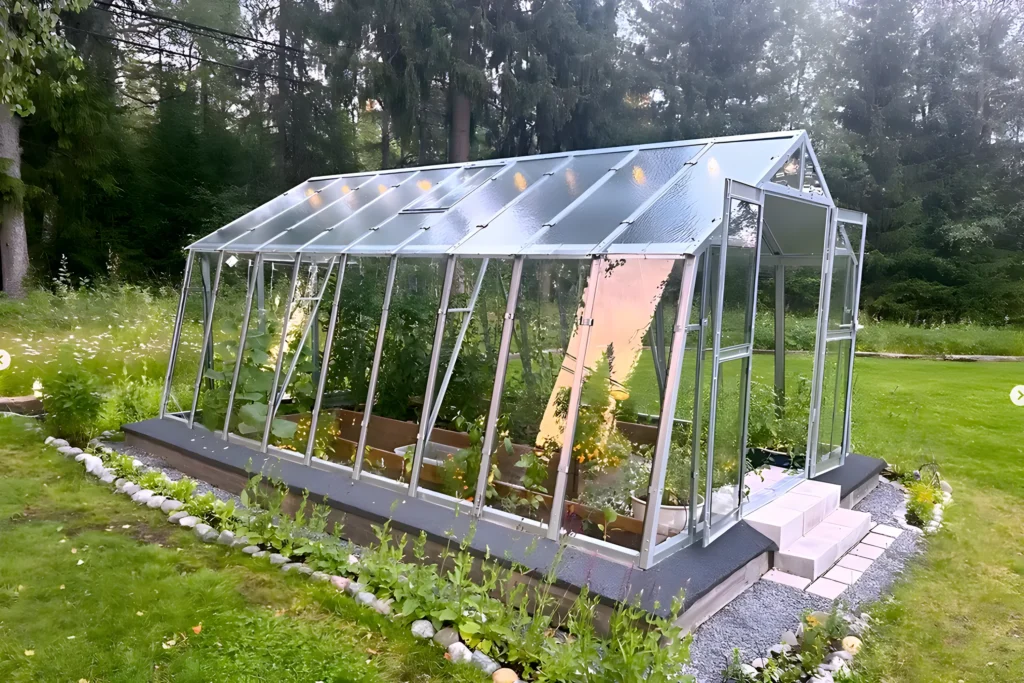 Grohus växthus Variant 303 Modell L från sidan med lutande glasväggar, takfönster och odlingsbäddar inne i växthuset, framför skog.